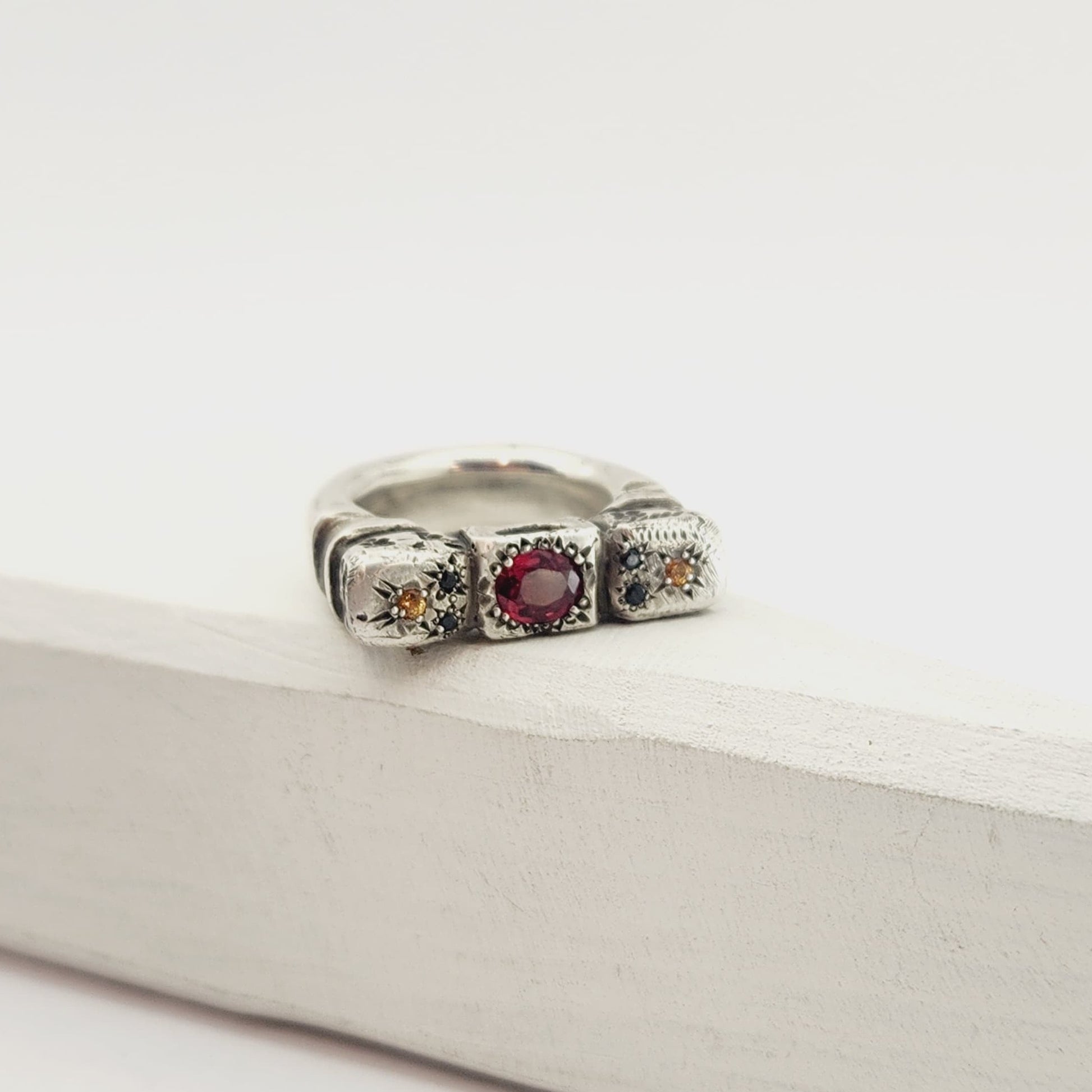 The Ruins Ring by Vaune Mason echoes anciant architectural colomns cast in chunky sterling silver. This ring is set with an oval red spinel at the centre, and on either side are small golden sapphires with two tiny black spinels. 