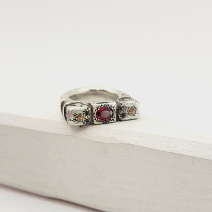 The Ruins Ring by Vaune Mason echoes anciant architectural colomns cast in chunky sterling silver. This ring is set with an oval red spinel at the centre, and on either side are small golden sapphires with two tiny black spinels. 