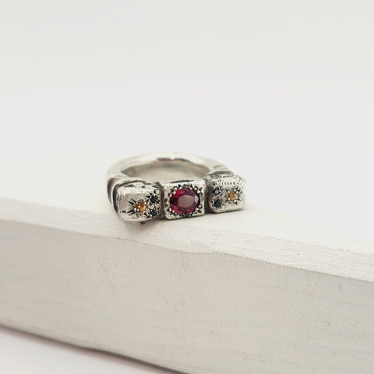 The Ruins Ring by Vaune Mason echoes anciant architectural colomns cast in chunky sterling silver. This ring is set with an oval red spinel at the centre, and on either side are small golden sapphires with two tiny black spinels. 