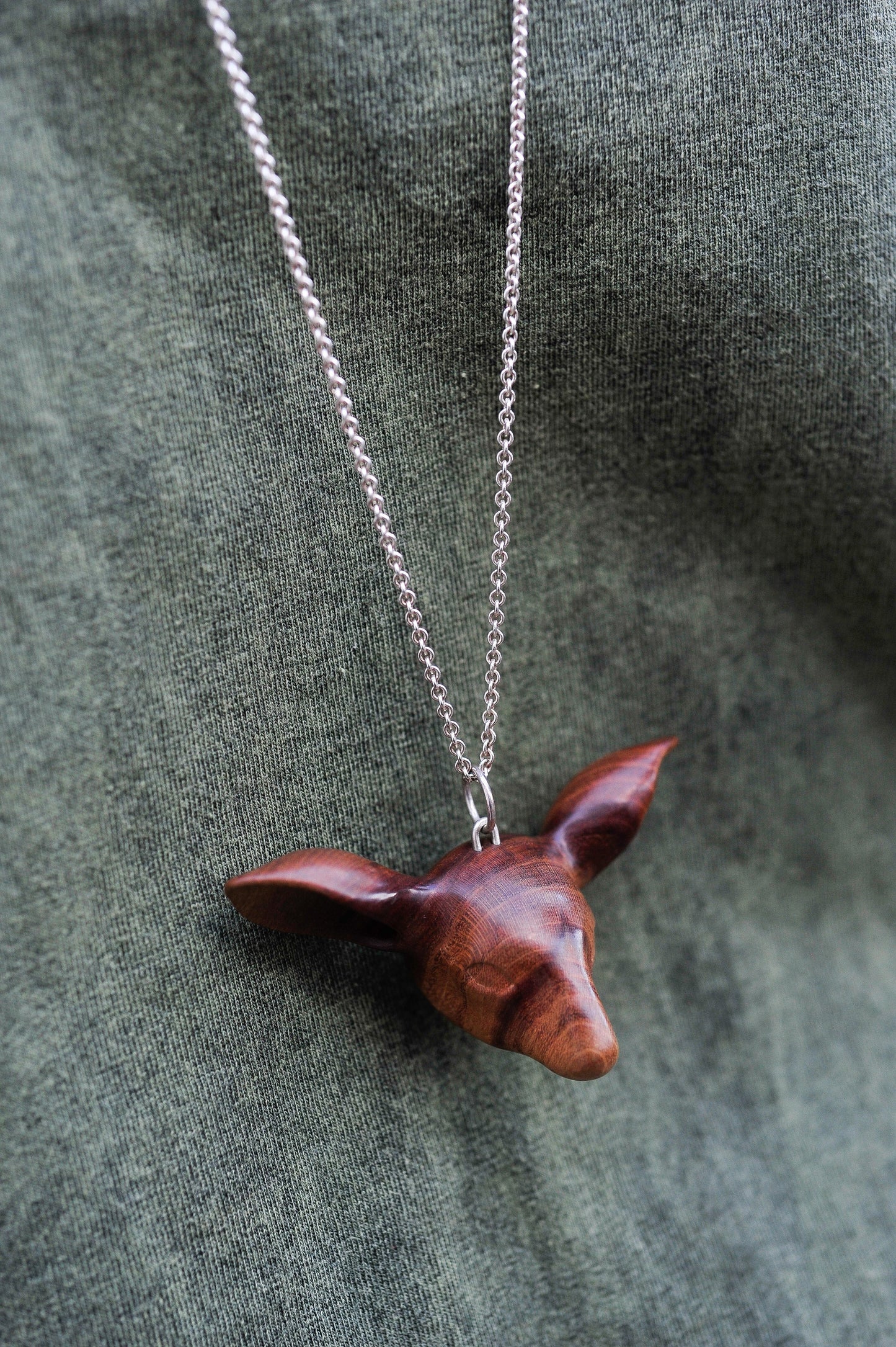The Doe's Head Necklace is hand carved in richly coloured cherry wood, finished with oils and beeswax and hung on a long solid sterling silver chain. Crafted by NZ jeweller Vaune Mason.