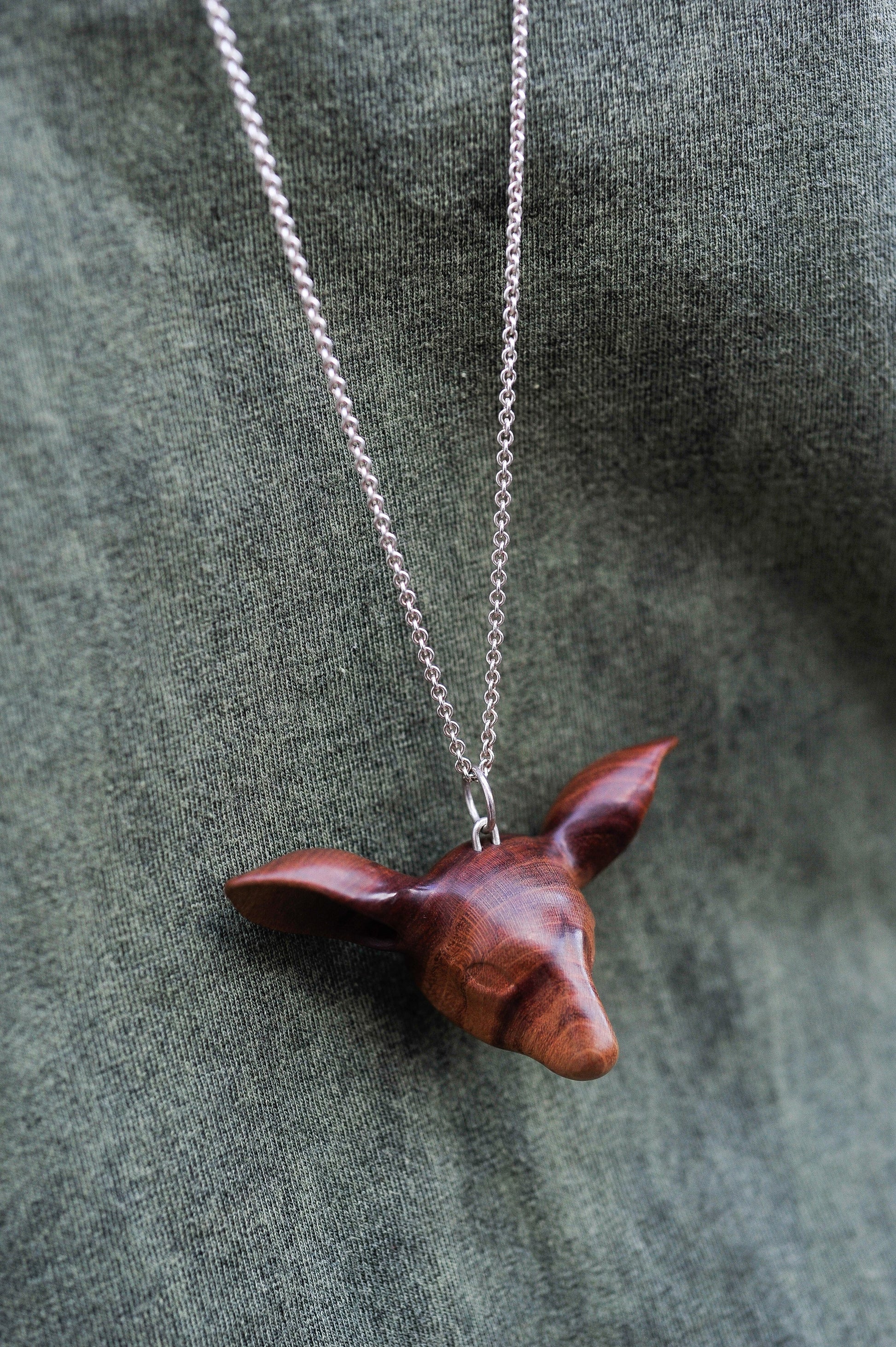 The Doe's Head Necklace is hand carved in richly coloured cherry wood, finished with oils and beeswax and hung on a long solid sterling silver chain. Crafted by NZ jeweller Vaune Mason.
