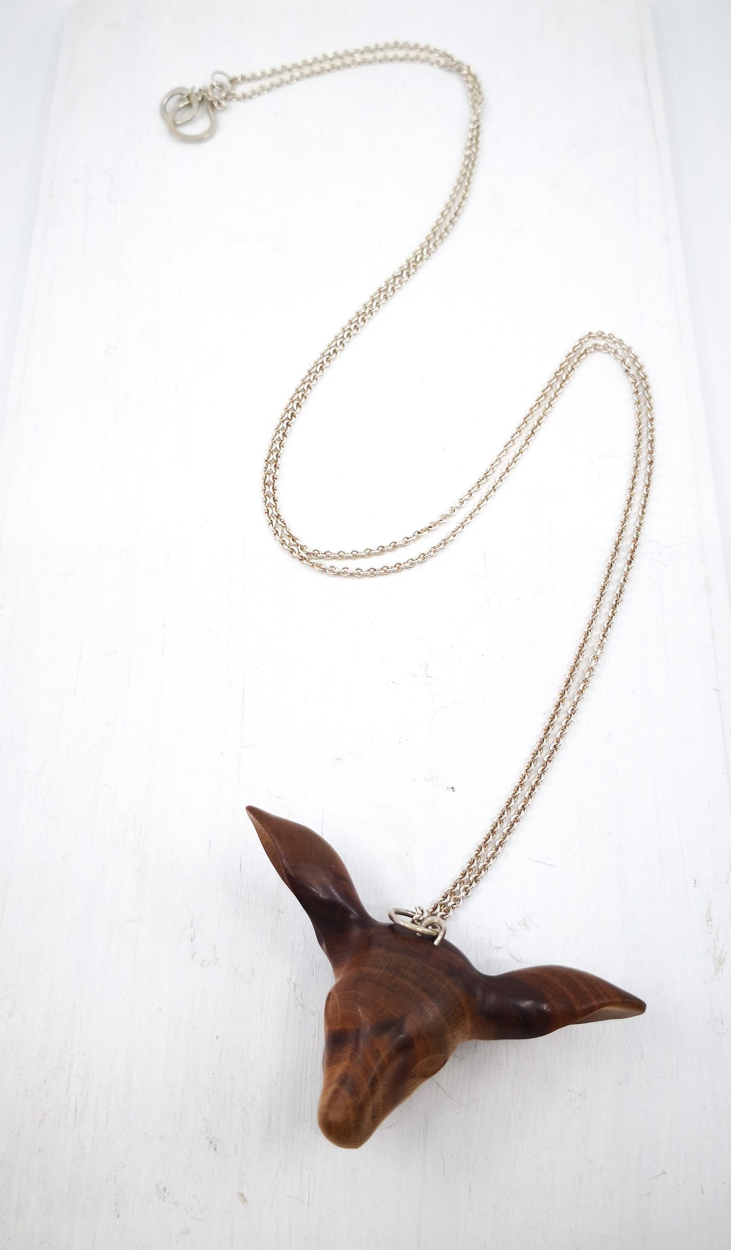 The Doe's Head Necklace is hand carved in richly coloured cherry wood, finished with oils and beeswax and hung on a long solid sterling silver chain. Crafted by NZ jeweller Vaune Mason.